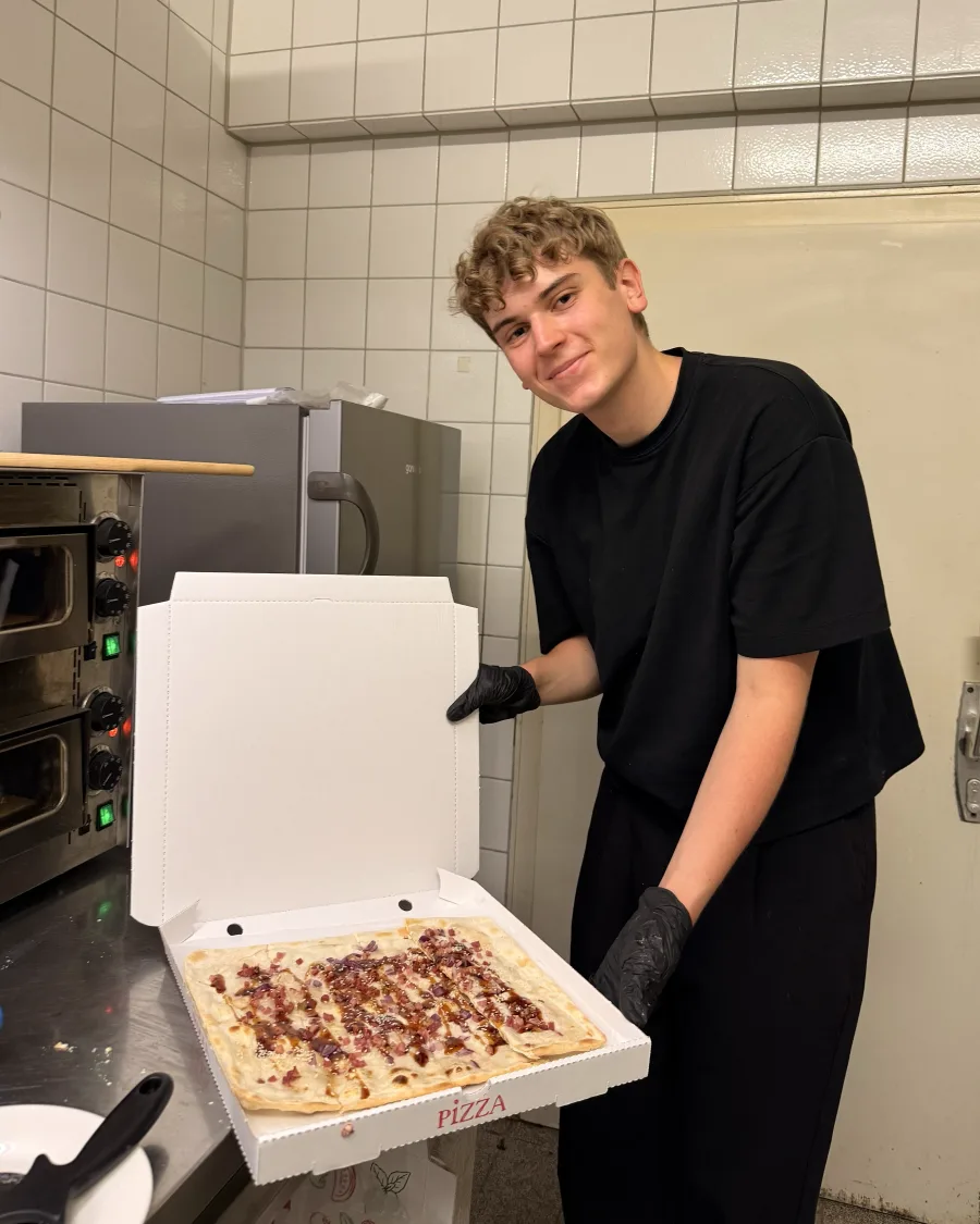 Moritz präsentiert einen frischen Flammkuchen in der Küche der Ma Bar